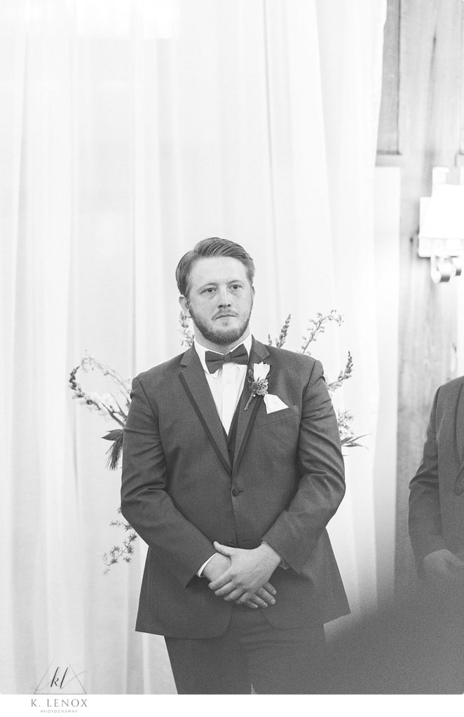Black and white photo of a groom waiting for his bride to walk down the aisle. 