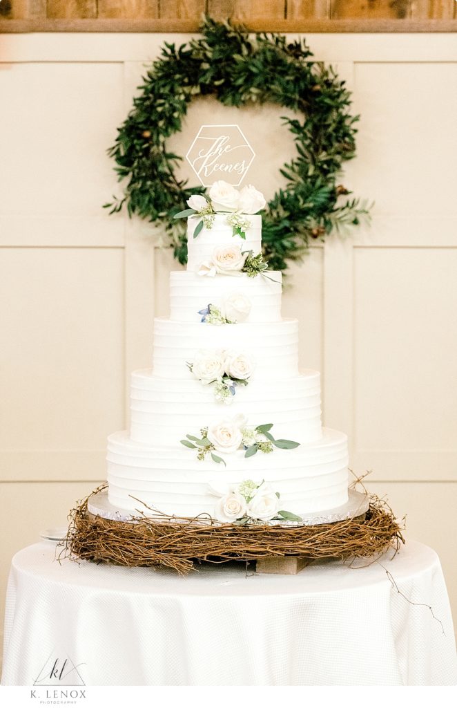 5 Tiered simple white wedding cake with light colored flowers. 