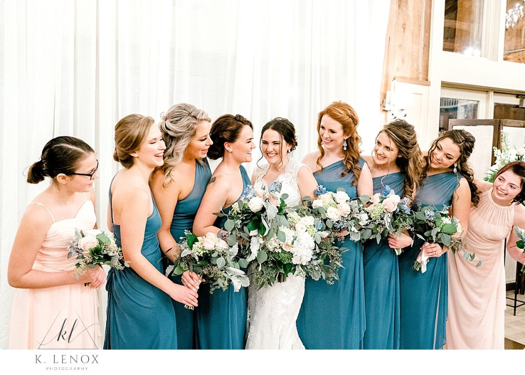 A bride with her bridesmaids wearing blue dresses inside the Barn at Gibbet Hill. 