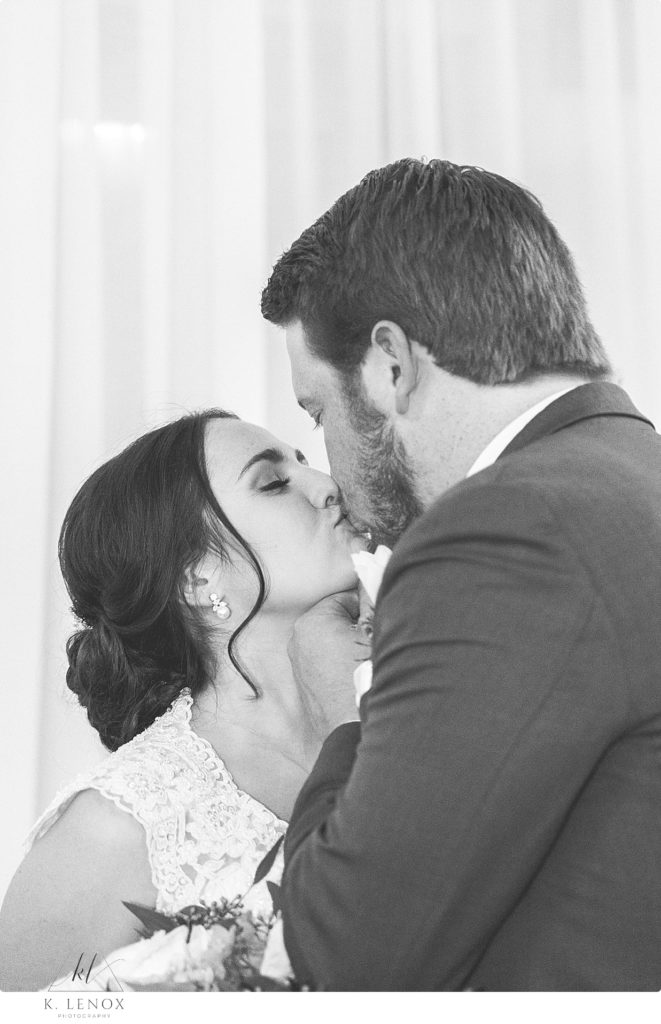 Black and white candid photo of a bride and groom sharing a kiss. 