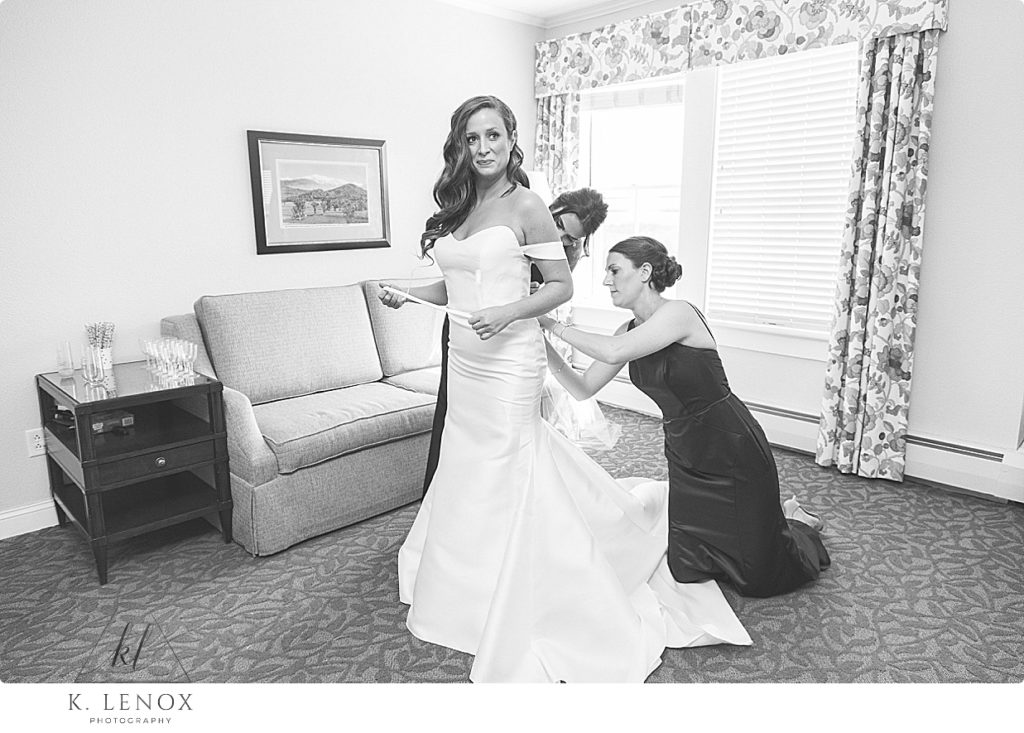 Black and White photo of a bride getting into her wedding dress with the help of two bridesmaids. 