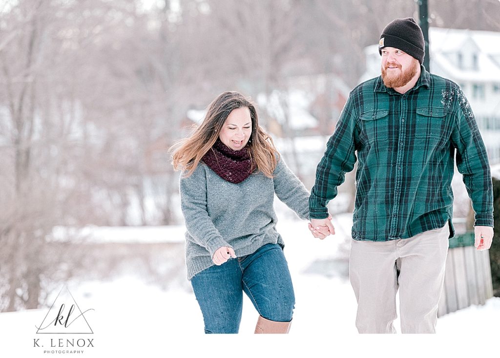 Winter Engagement Session in Peterborough NH- man and woman playfully walk in the snow holding hands. 