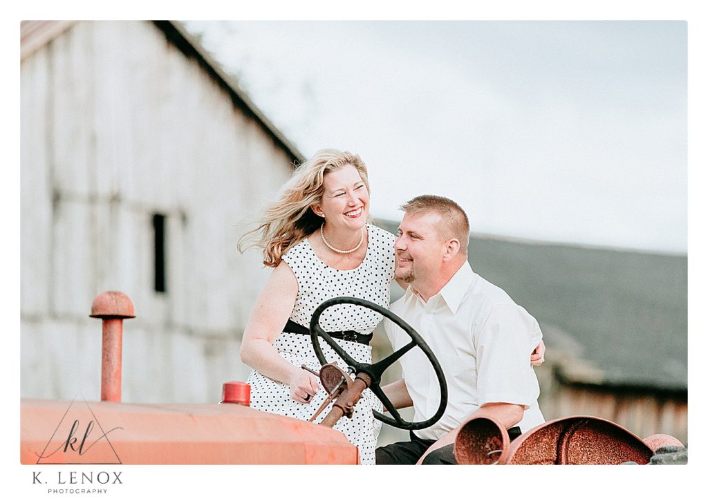 Candid photo of a man and woman sitting on a tractor and being silly and laughing. 