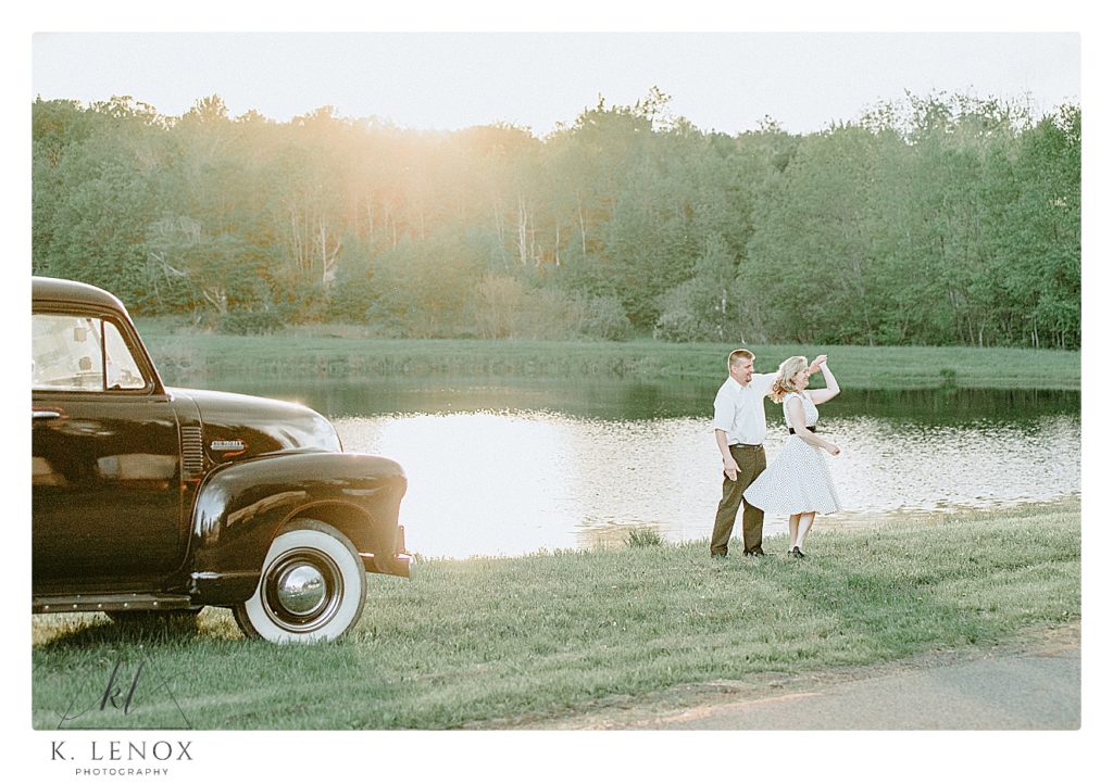 Man and Woman dance in front of a pond with the sun shining behind them.  There is a black 1952 Chevy Truck in the photo too. 