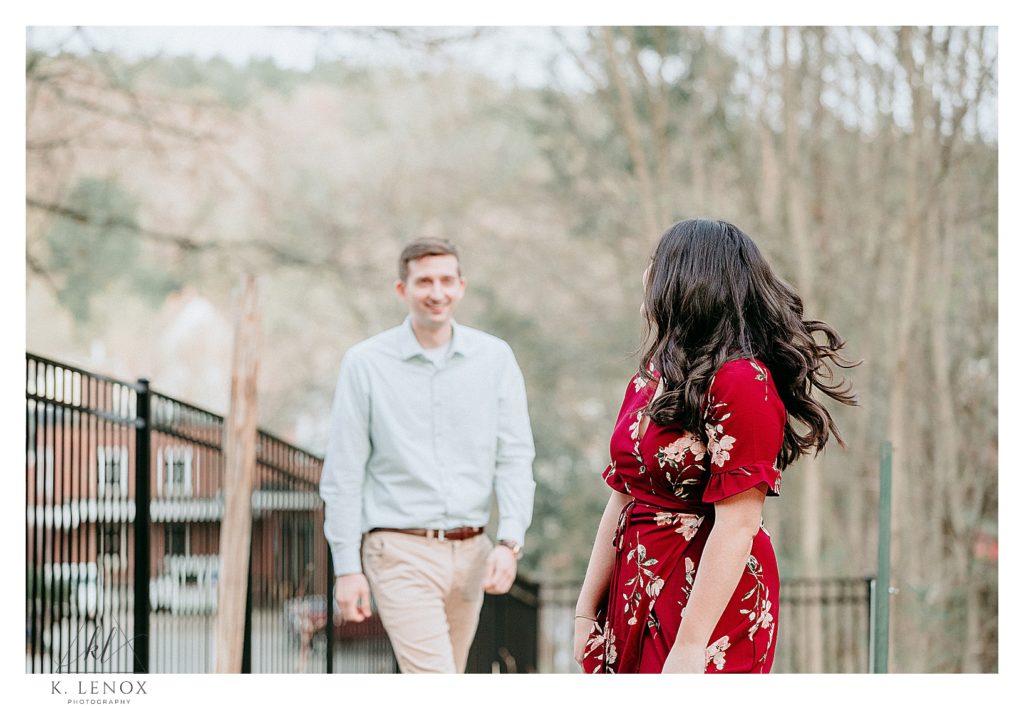 Candid,  light and airy photograph taken in Peterborough NH during their engagement session.  Woman wearing a Red floral dress and a Man wearing a light blue button down shirt. 