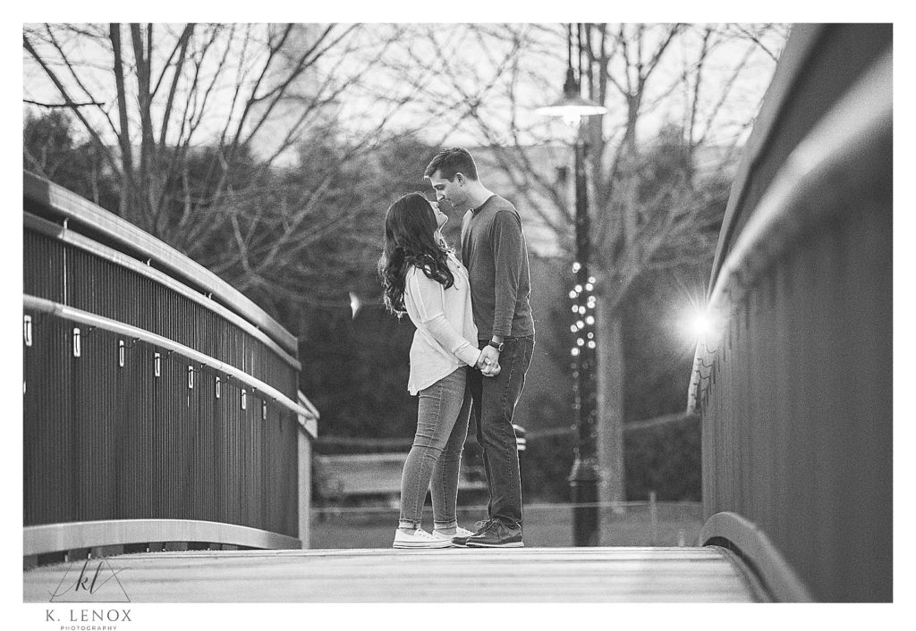 Black and White photo of a man and woman crossing a walking bridge in Peterborough NH during their spring engagement session. 
