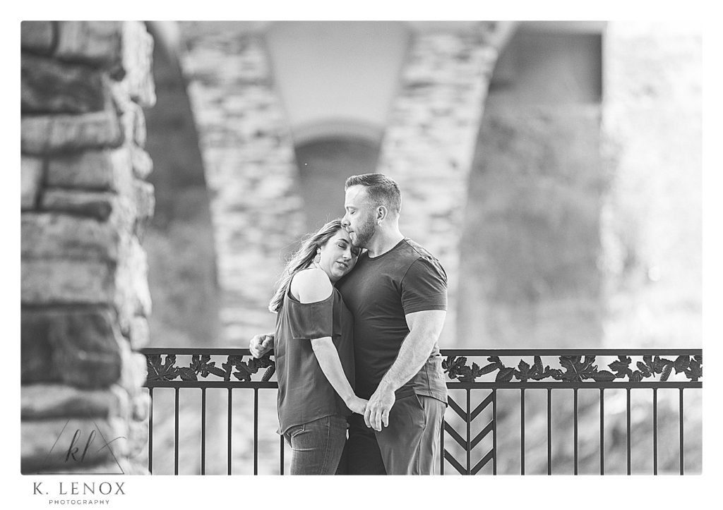 Black and White photo of a Relaxed Engagement session in Brattleboro VT with a Man and Woman, embracing under a bridge overlook. 