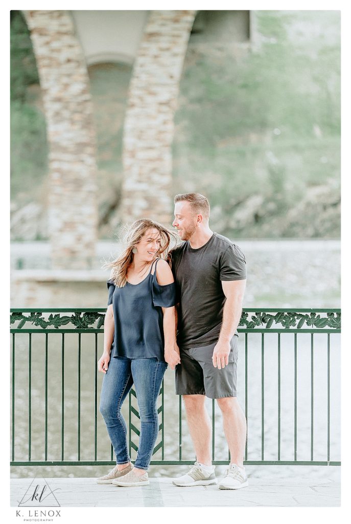 Candid photo of couple on a bridge overlook with the wind blowing her hair all over for a natural image. 