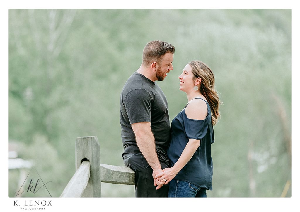 Light and Airy photo of an engaged couple holding hands while leaning against  wooden fence during their engagement photos. 