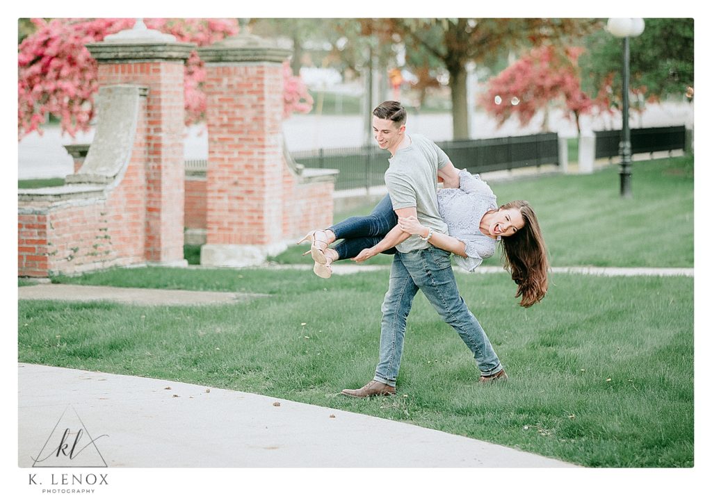 Playful man and woman laughing during their spring engagement session in Keene NH.  Man picks woman up and tosses her around playfully. 