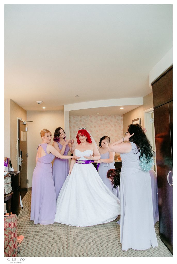 Bridesmaids help the bride in her wedding gown while being silly. 
