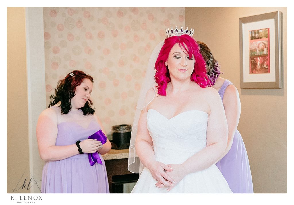 Bride with red hair and a crown gets ready with the help of her bridesmaids on her wedding day. 