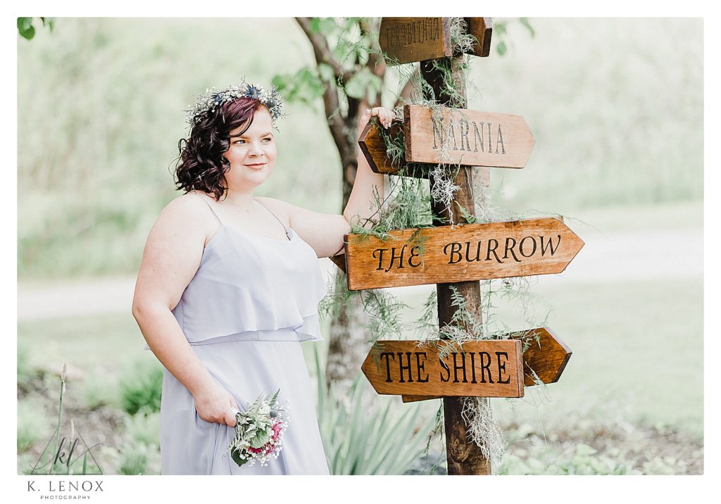 Bridesmaid poses with a wooden arrow sign on a wedding day with an enchanted forest Theme with a Game of Thrones Twist. 