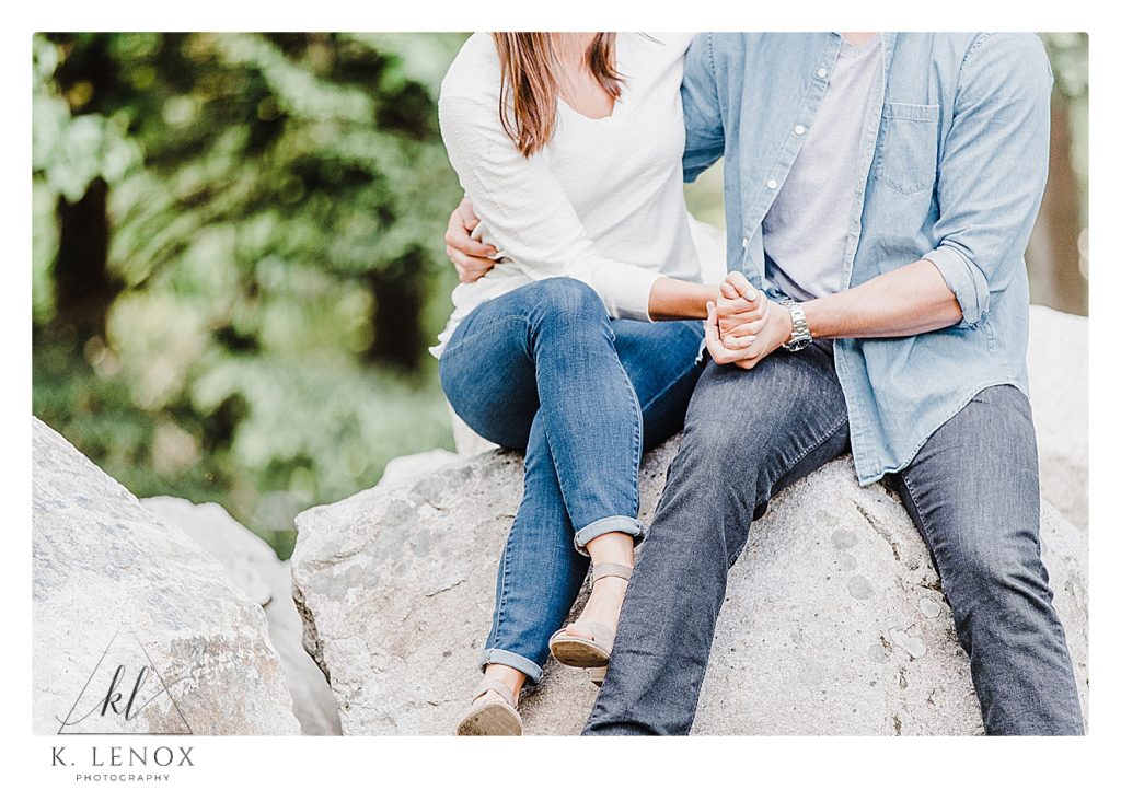 Close up photo of A couple wearing jeans and white shirts while sitting on a rock.  (Detail Photo)