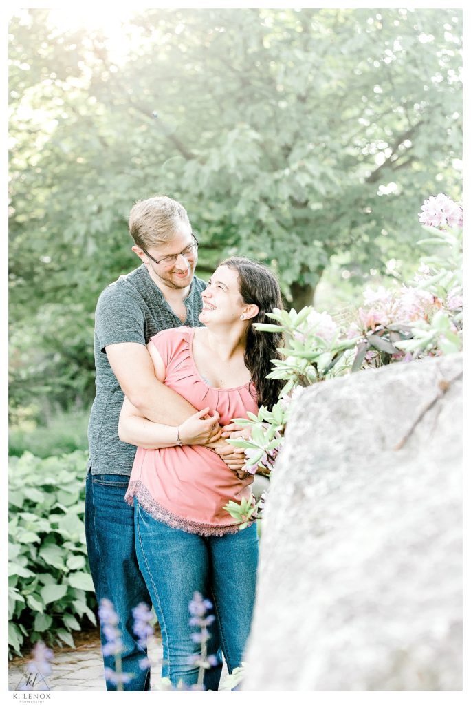 Light and Airy photo showing a woman wearing a pink blouse and blue jeans is getting hugged by her fiance during their Engagement Session. 