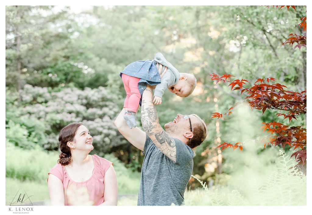 Light and Airy Family photo showing a dad lift his 10-month infant over his head while mom smiles. 