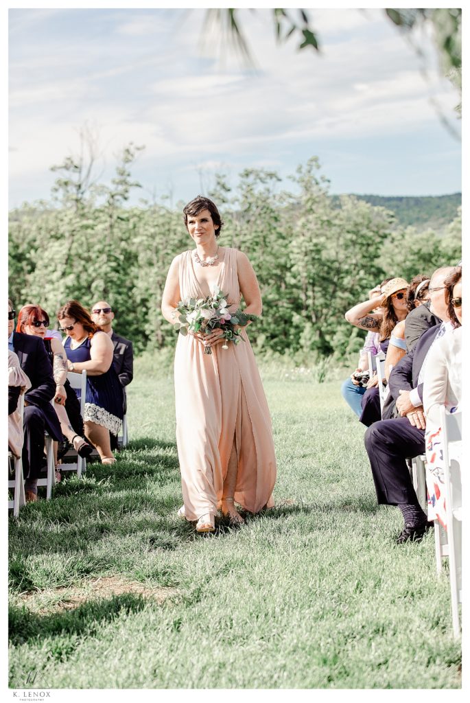 Bridesmaid wearing a pale, dusty rose dress walks down the aisle at the Mayfair Farm Wedding in Harrisville NH. 