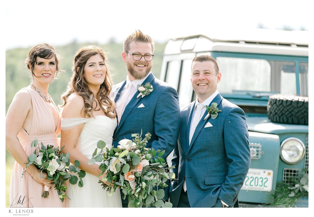 Small Wedding party poses for a photo in front of an Antique Land Rover. 