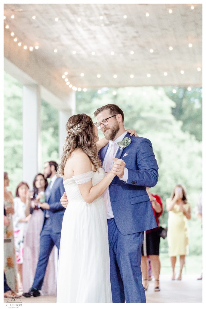 Light and airy photo of a bride and groom having their first dance on the covered porch of Mayfair farm. 