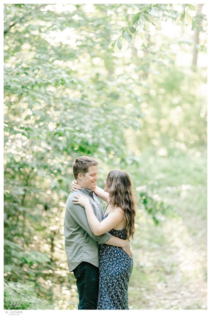 Man and woman have an outdoor engagement session in Brattleboro vt.  They are hugging surrounded by trees. 