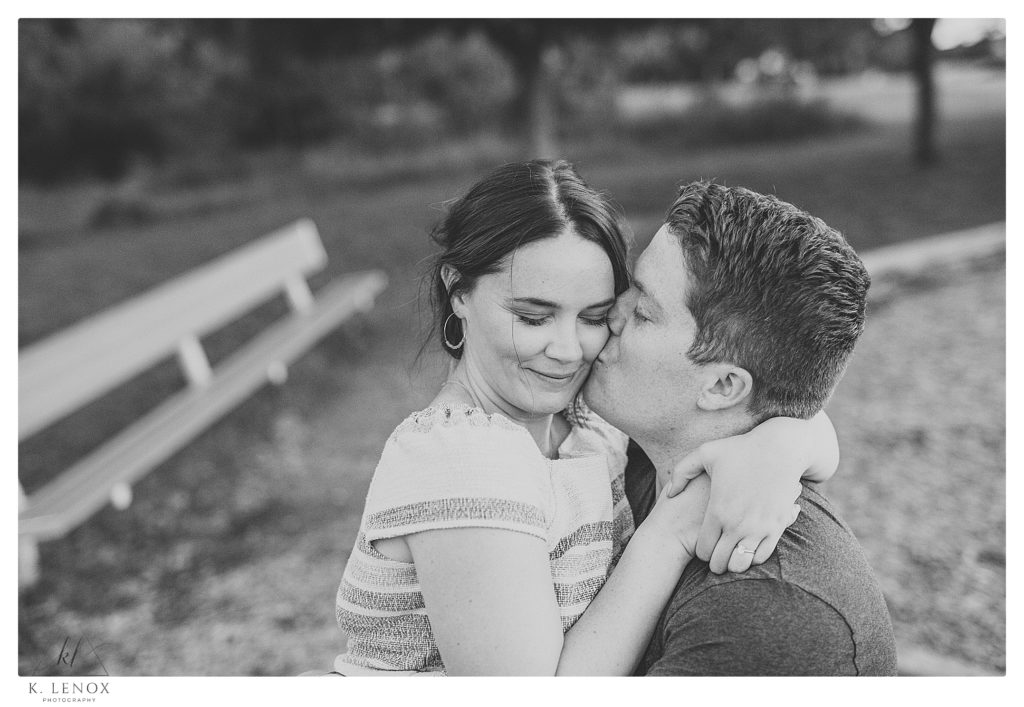 Black and White photo of a man and woman cuddling at the Park during their engagement session with K. Lenox Photography. 