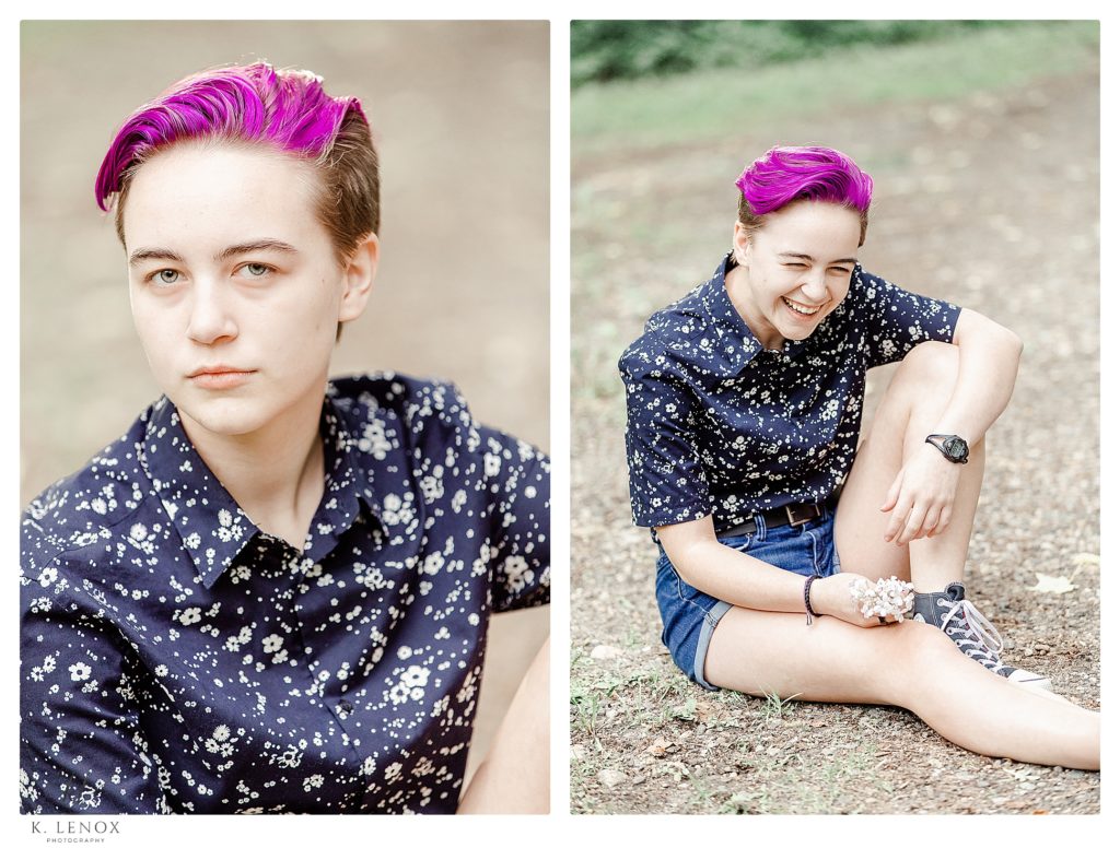 Portrait of a girl sitting on the ground.  She has Purple hair, and wearing a black floral button down shirt.  
