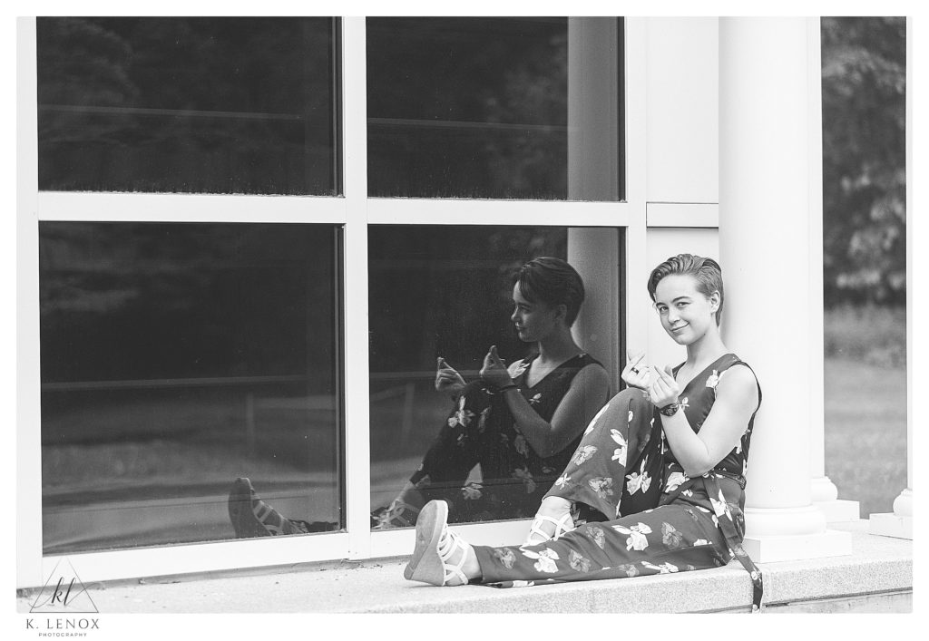Black and White photo showing a girl sitting next to a window that shows her reflection during a senior portrait session in VT. 