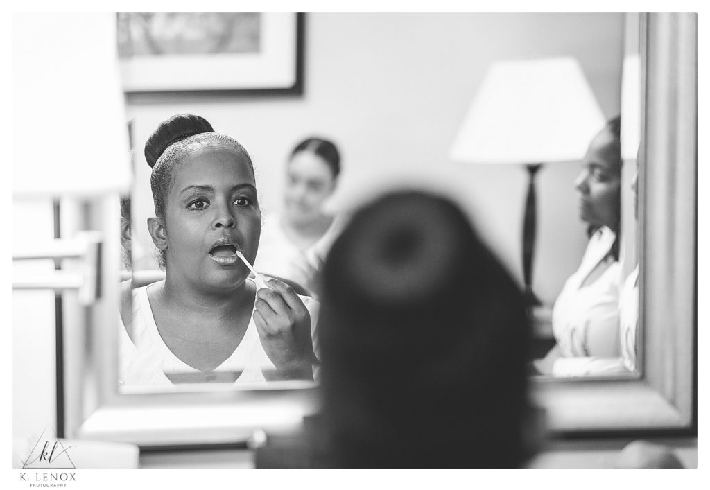Black and white photo of a woman applying lip gloss in the mirror. 