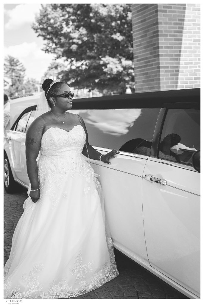 Black and White photo of a bride standing next to a limo before heading to her classic wedding at the Alpine Grove. 