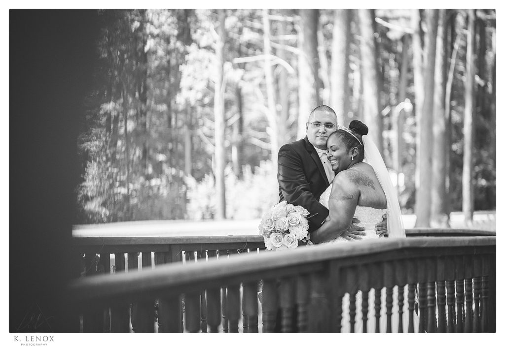 Candid and joyful black and white photo of a bride and groom hugging on the wooden bridge at Alpine grove. 