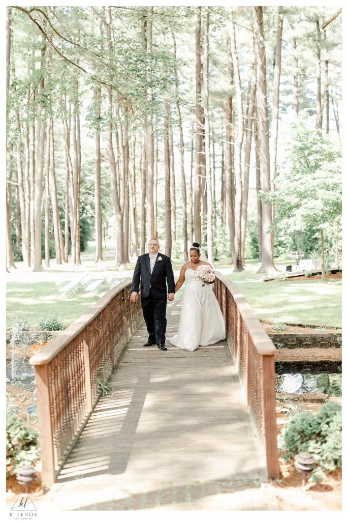 Bride and Groom walk hand in hand across the wooden bridge at Alpine Grove in Hollis NH. 