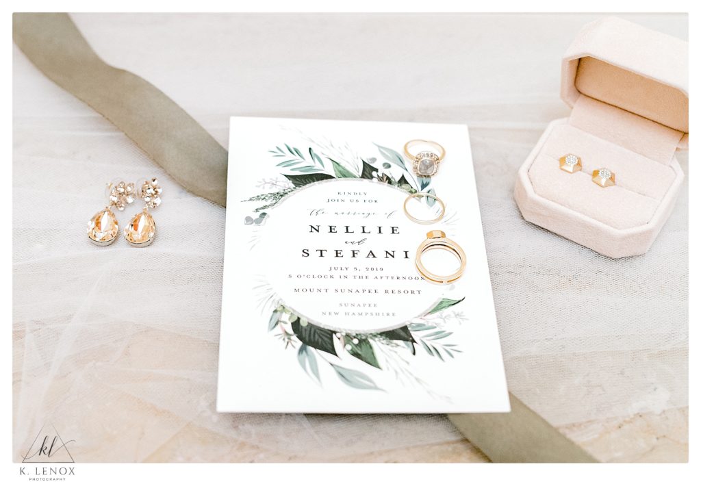 Light and Airy flat lay showing a simple classic white invitation with the wedding rings and two sets of gold earrings. 