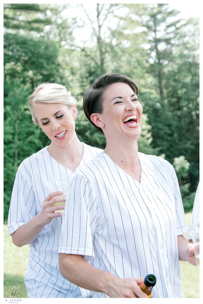 The two brides laugh while wearing their custom "getting ready" baseball Jerseys. 
