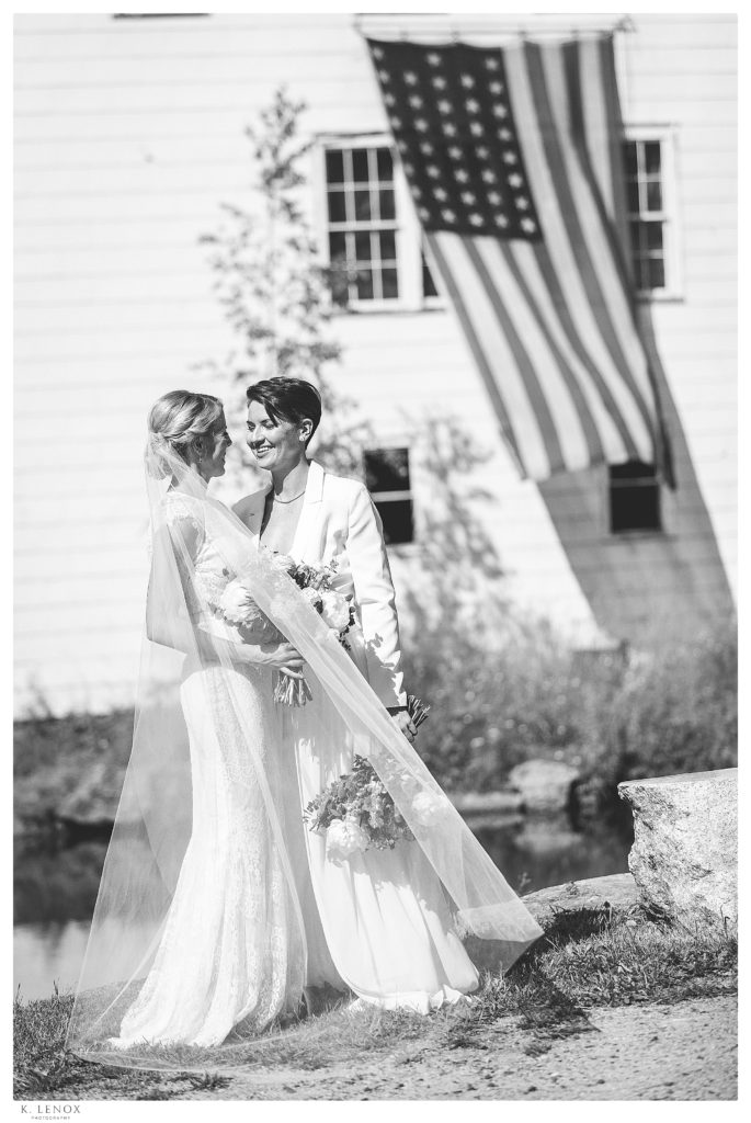 Black and white photo of two brides on their wedding day with an american flag in the back ground. 