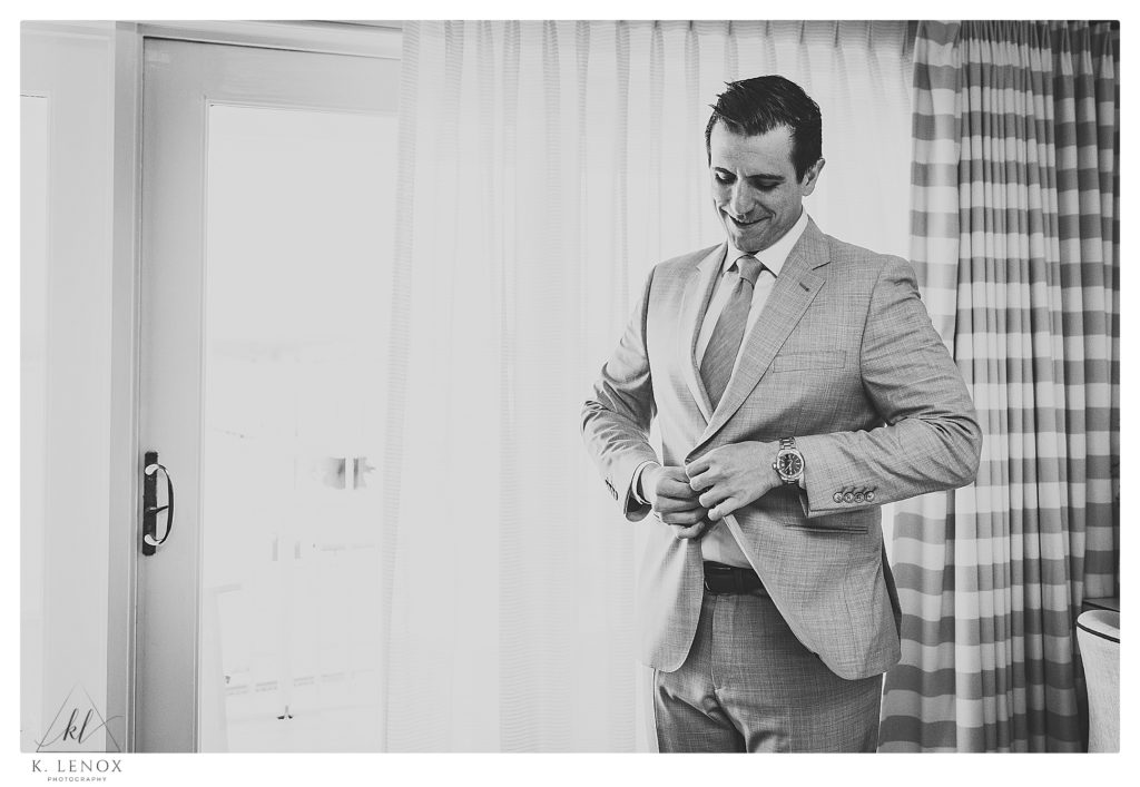 black and white photo of a groom buttoning his suite jacket on his wedding day. 