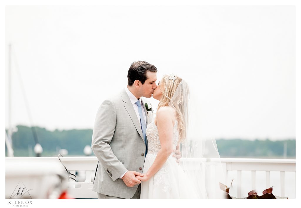 Bride and Groom kiss on the dock in front of the Wentworth by the Sea in NH.  Light and Airy photo. 