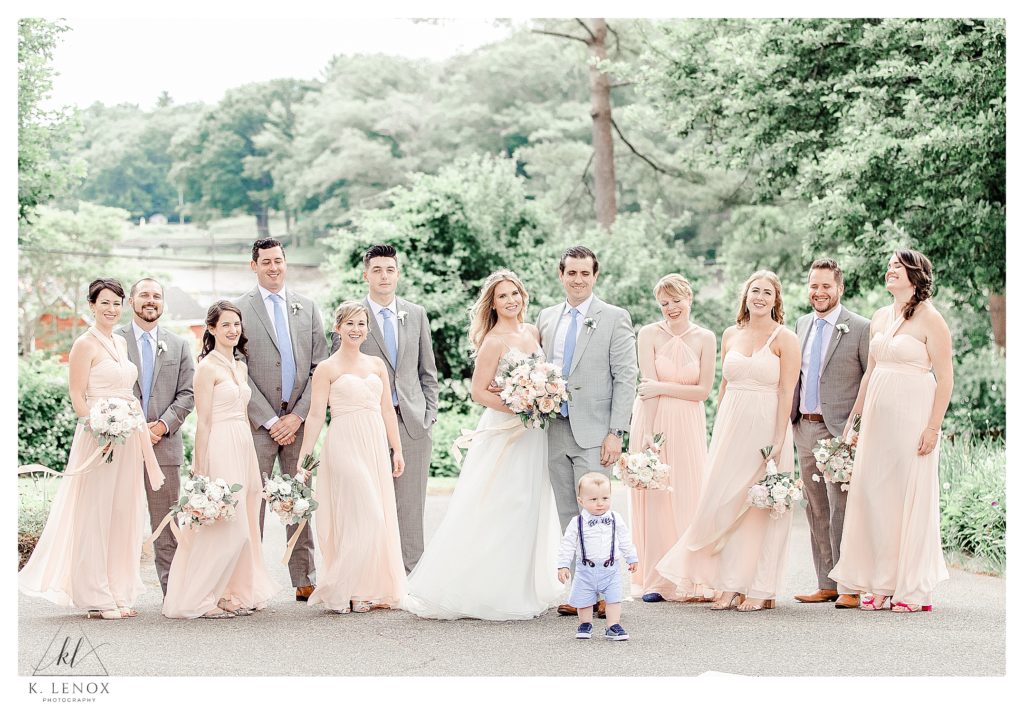 Entire wedding party, wearing light pink and gray, pose for a portrait at the York Golf and Tennis Club. 