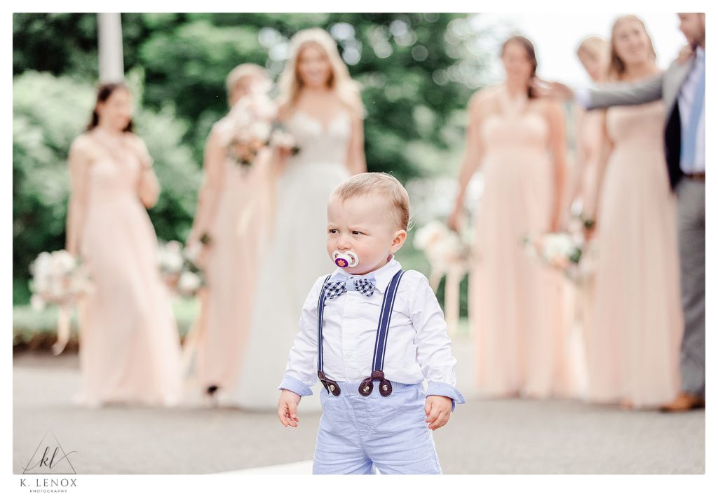 Young boy wearing suspenders and a bowtie has a photo taken in front of a wedding party at the York Golf and Tennis Club. 