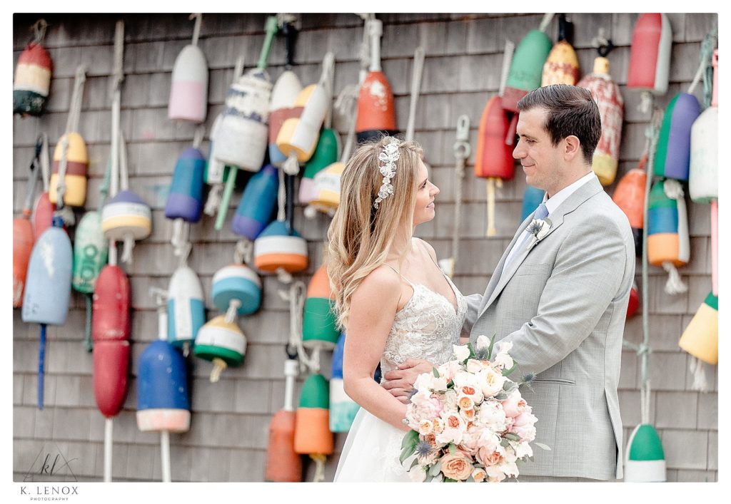 Candid photo of a bride and groom in front of a wall of colorful buoys for their wedding at the York Golf and Tennis Club in Maine. 