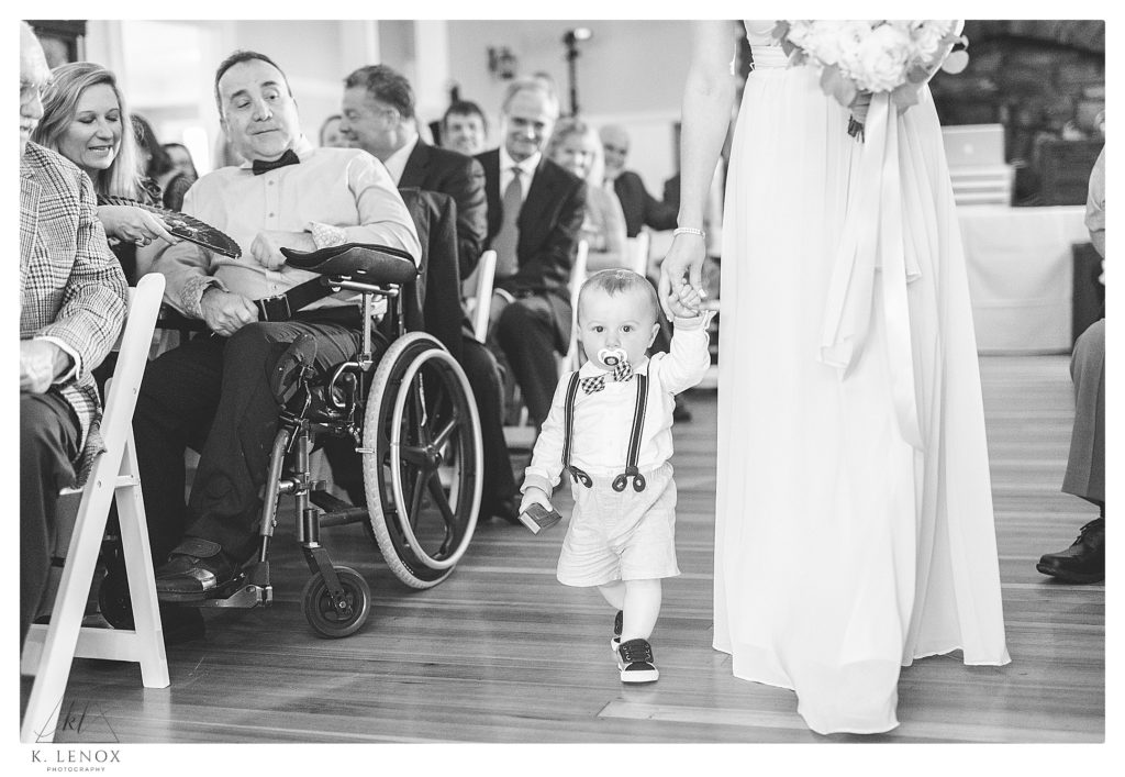 Black and White photo of a toddler walking down the aisle at the York Golf and Tennis Club, inside wedding ceremony. 