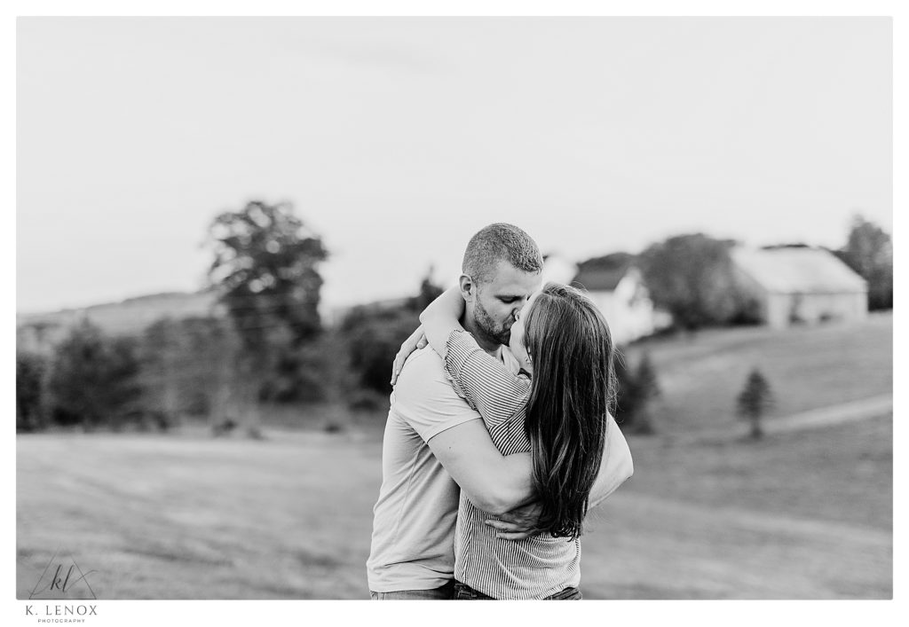 Black and White Photo of a Man and woman kissing during their engagement session at Cathedral of the pines, while overlooking the hills below. 