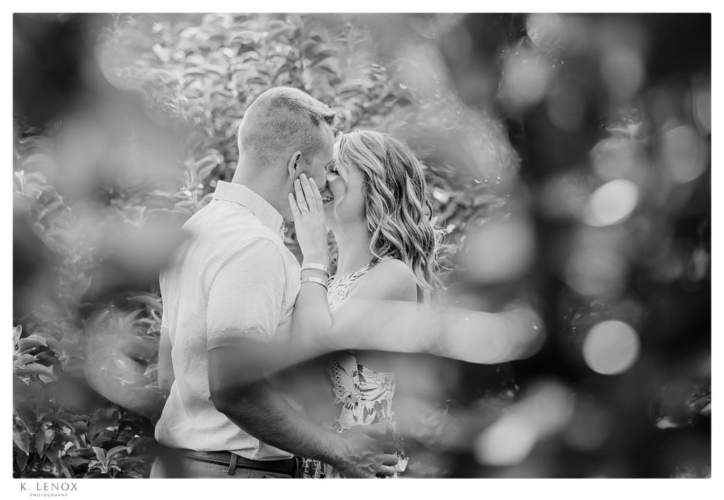 Black and White candid photo of a man and woman kissing through the leaves in Alyson's Orchard. 