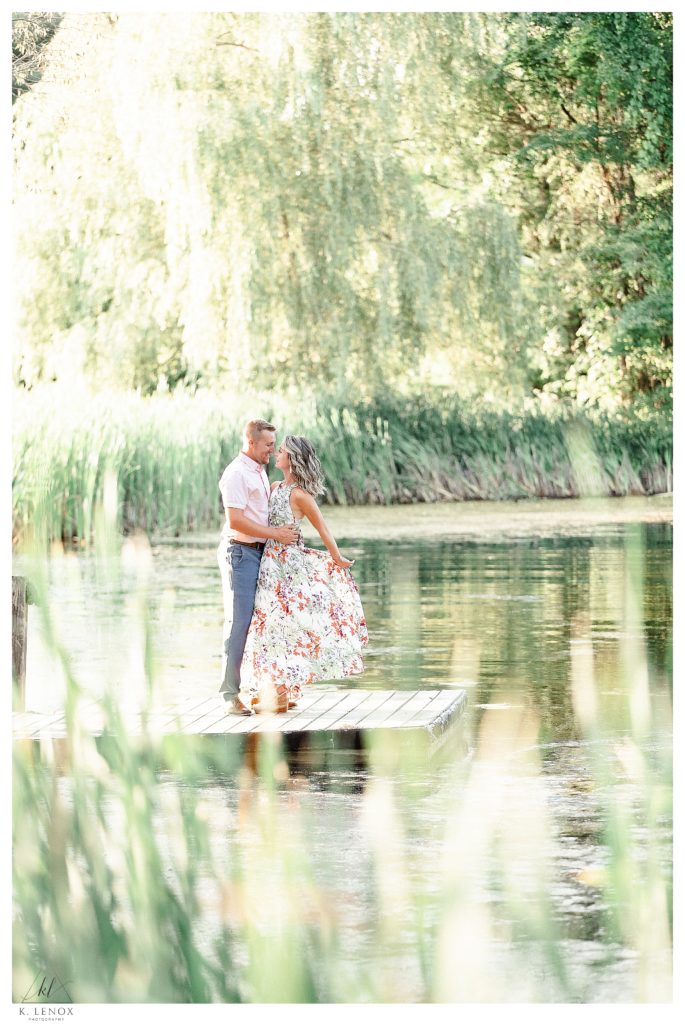 Light and Airy Engagement session at Alyson's Orchard showing a man and woman on the dock at the edge of the pond on a sunny summer evening. 