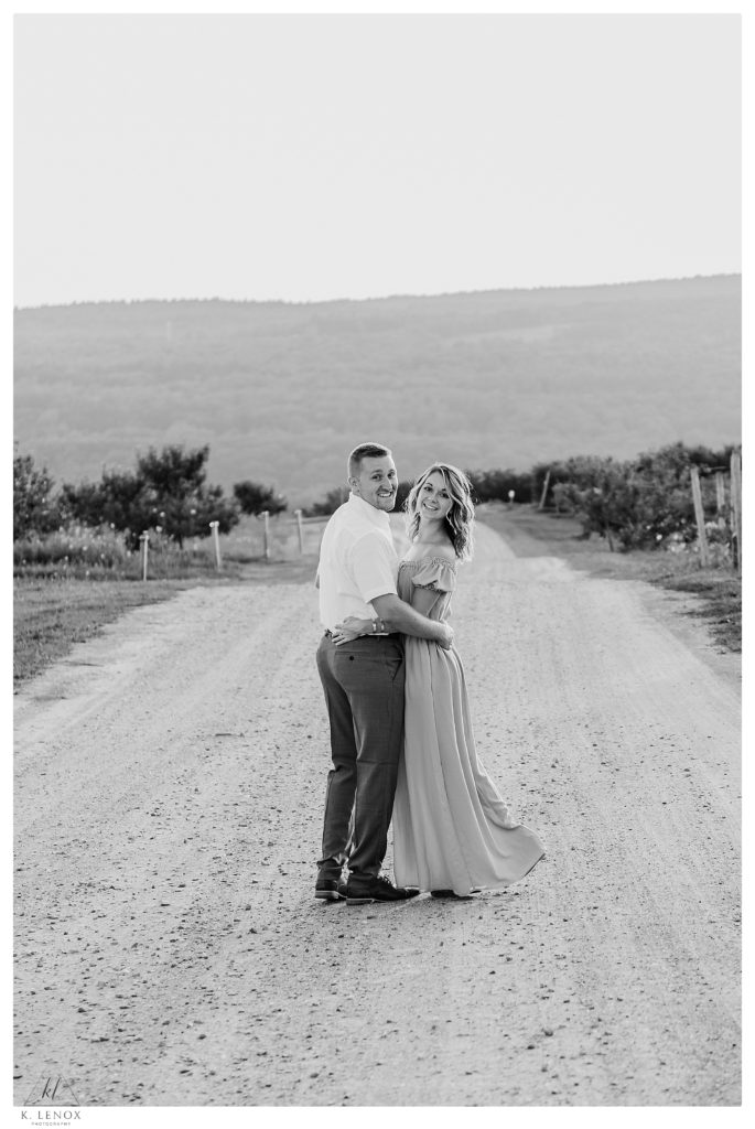 Black and White photo of a man and woman walking on the dirt road at Alyson's Orchard in Walpole NH during their engagement session. 