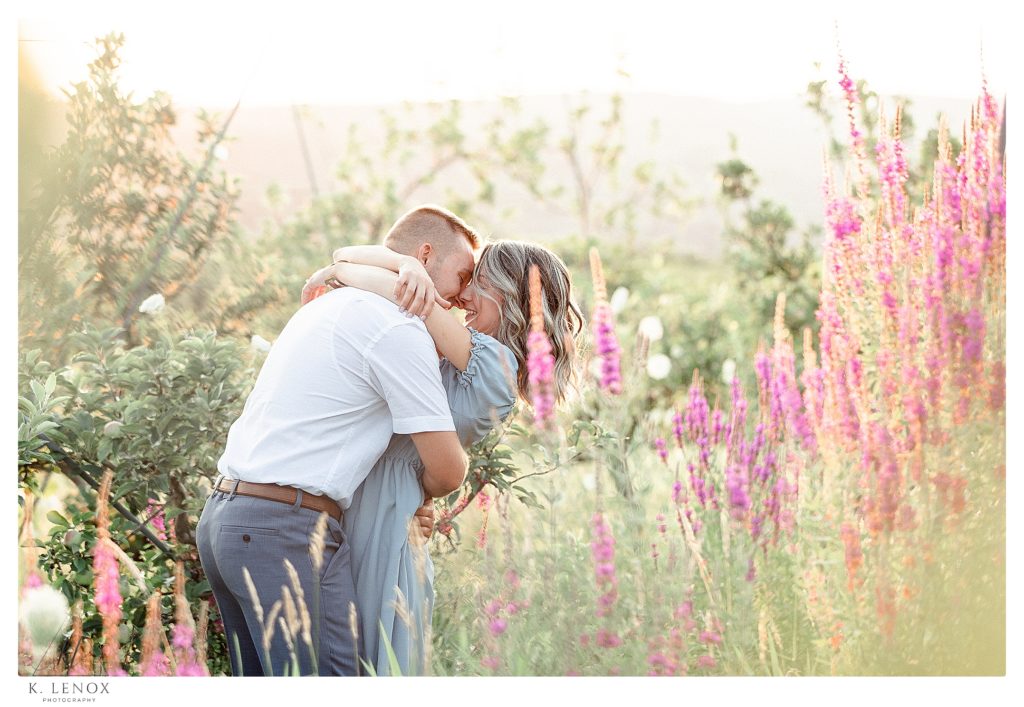 Light and Airy engagement session at Alyson's Orchard showing a pretty blonde woman standing in a field of purple flowers hugging. 