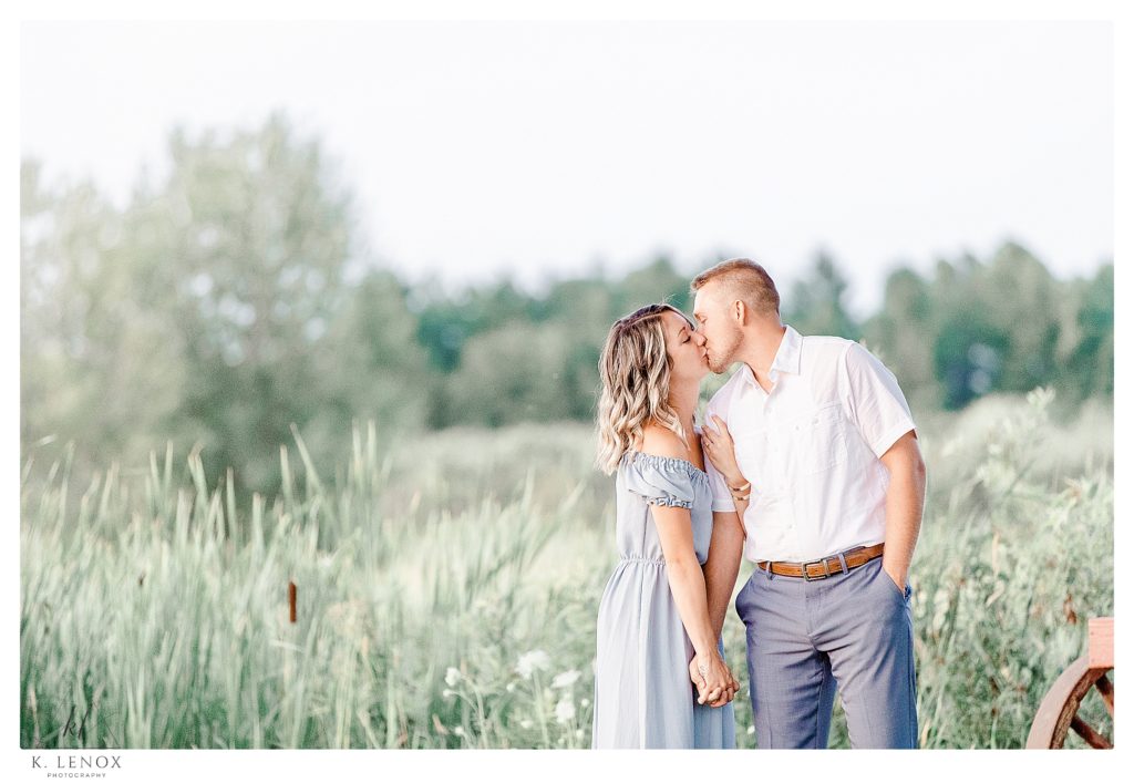 Light and Airy engagement session at Alyson's Orchard showing a pretty blonde woman kissing her fiance in a field of green grasses. 
