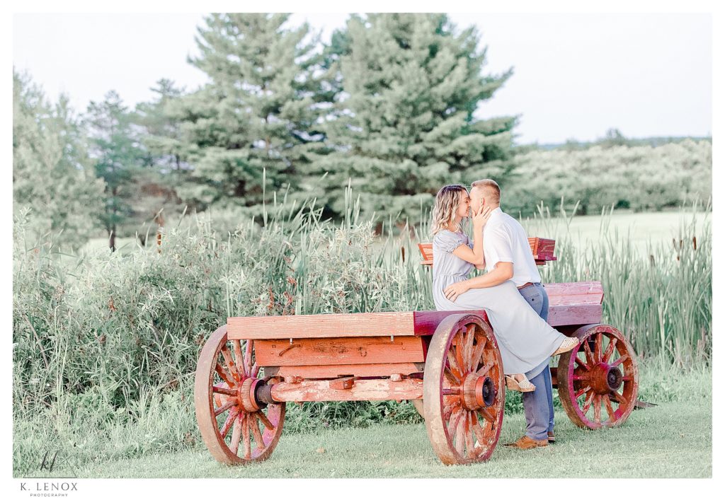 Light and Airy engagement session at Alyson's Orchard showing a pretty blonde sitting on a red wagon kissing her fiance. 