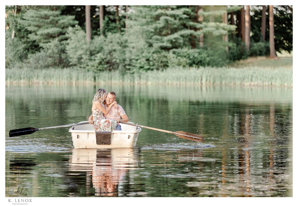 Man and Woman laugh on a row boat ride on a pond at Alyson's Orchard in Walpole NH.  Light and Airy Engagement Session. 