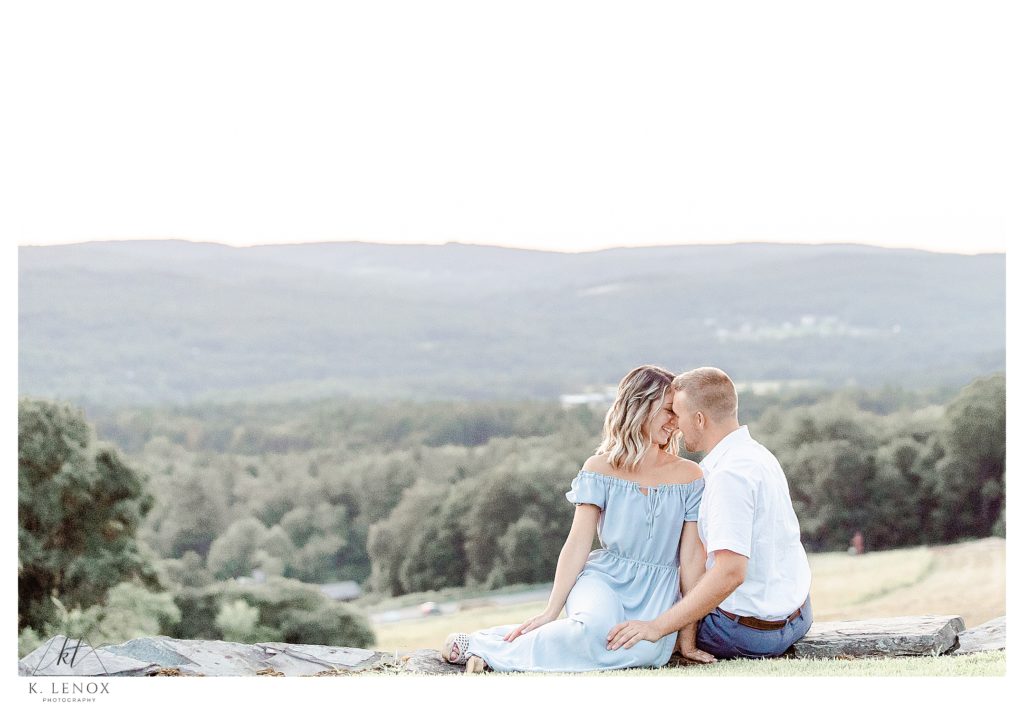 An engaged couple sit on a rock wall at Alyson's Orchard and enjoy the view of the CT valley during their light and Airy Engagement session with K. Lenox Photography. 