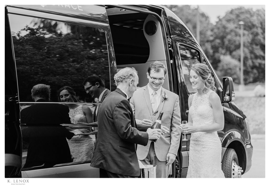 Black and White photo of a bride and groom having a champagne toast outside the limo bus. 